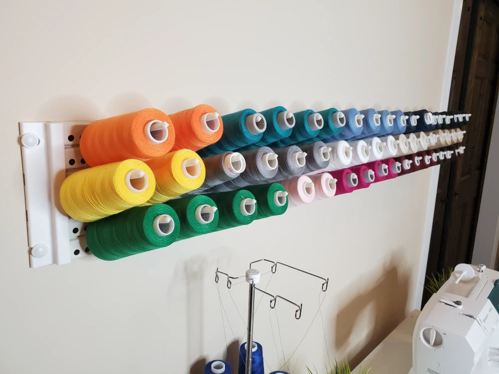 A cream with white trim Handypeg pegboard product shown organizing multiple spools of thread in a sewing room.